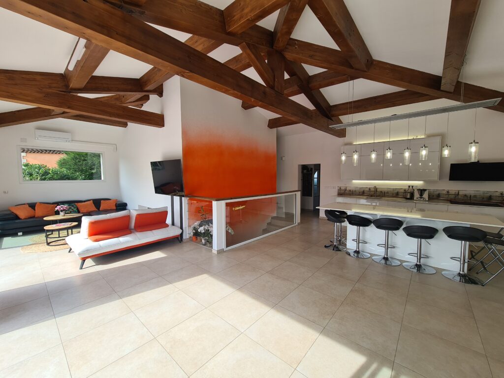 Grande pièce de vie avec cuisine ouverte, charpente apparente et salon après la transformation d'une ancienne piscine intérieure en loft à Châteauneuf-les-Martigues.