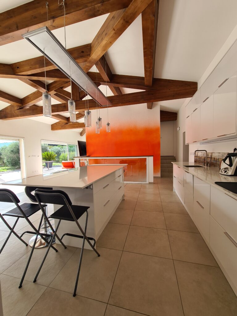 Cuisine contemporaine blanche avec îlot central et charpente apparente après la transformation d'une ancienne piscine intérieure en loft à Châteauneuf-les-Martigues.